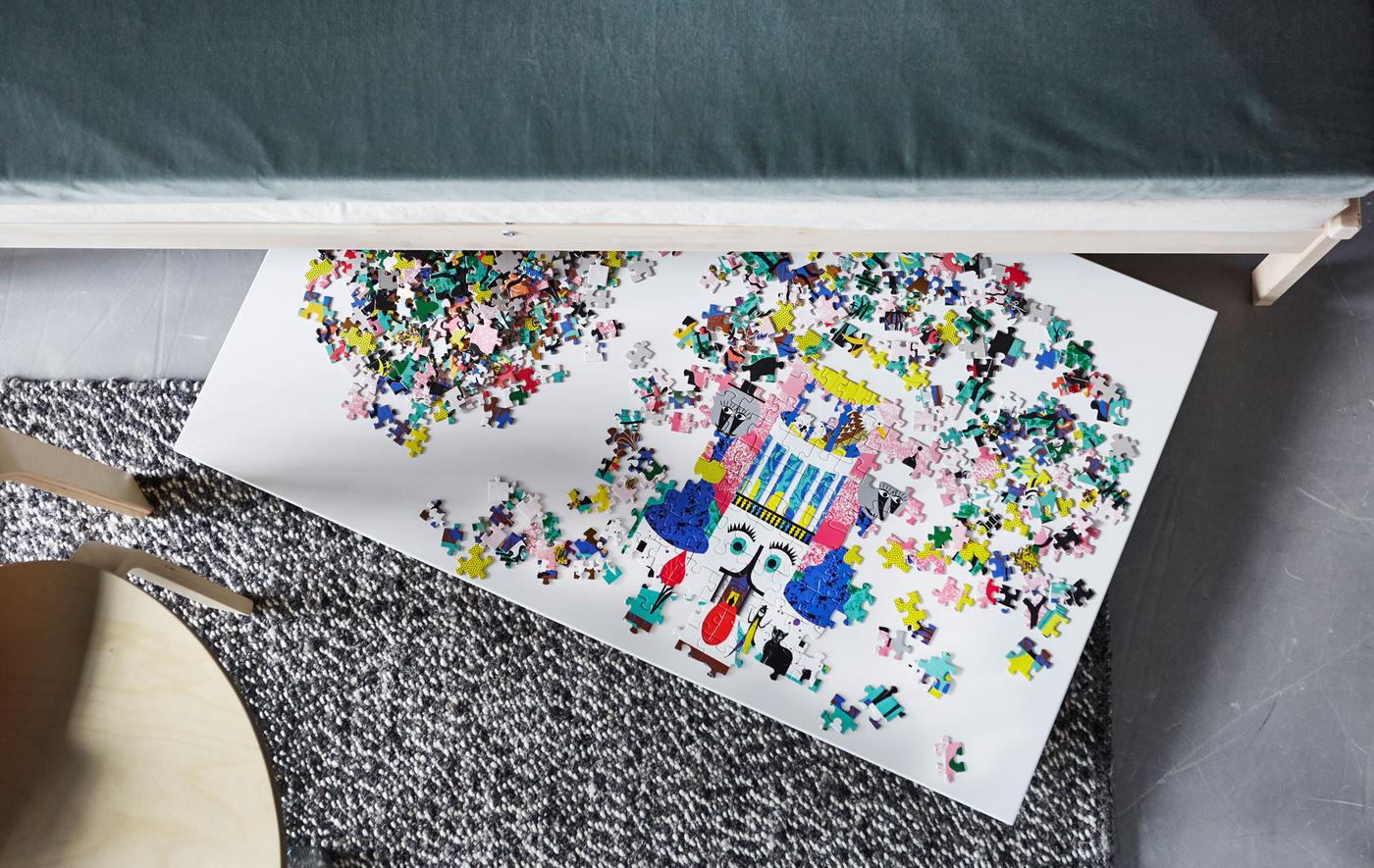 An overhead view of a puzzle on a board that’s sticking out from under a sofa.