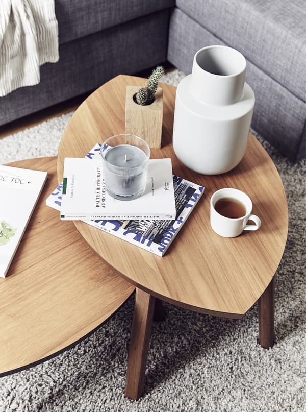 An overhead view of two leaf-shaped coffee tables with a white vase, candle, and mug of coffee.