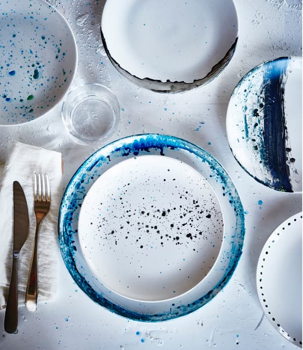 An overhead view on of white IKEA FÄRGRIK plates that have been painted with different designs in shades of blue.