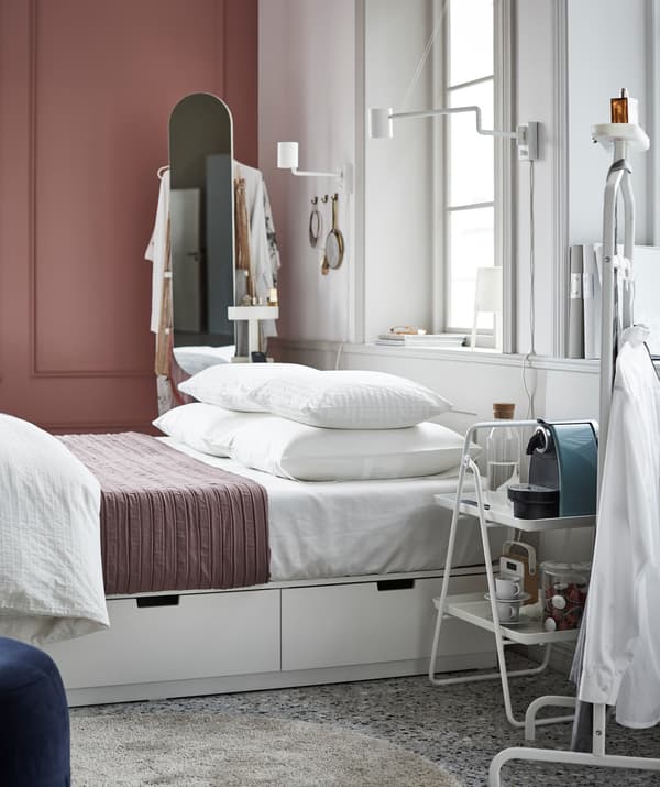 An ultra-organised bedroom with an IKEA NORDLI bed frame with built-in storage and neatly stacked bed pillows.