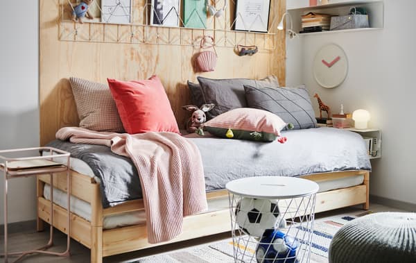 An UTÅKER stackable bed with lots of cushions and textiles on, surrounded by a bedside table, storage and decorations.
