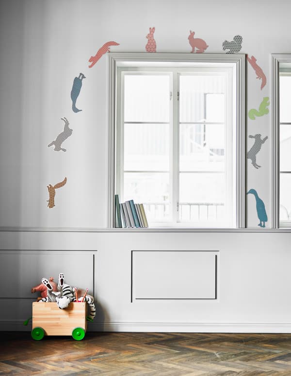 Animal-shaped stickers are placed to look as though they are running over the windown and down to a toy box on the floor.