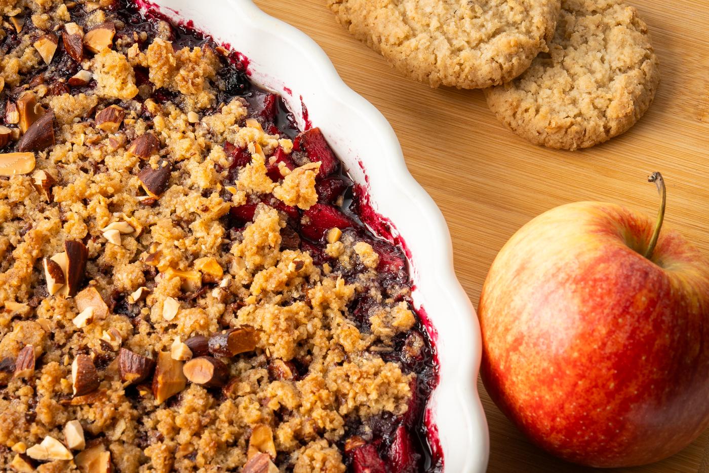 Apfel-Blaubeer Crumble in einer Auflaufform auf einem Schneidebrett präsentiert.