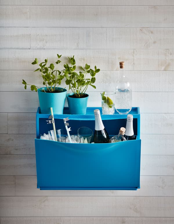 Armoire à chaussures bleue IKEA TRONES remplie de glace, de verres et de bouteilles de champagne, avec des plantes au-dessus.