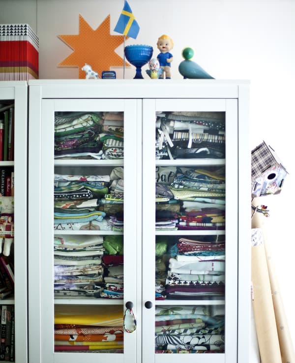Armoire blanche avec portes vitrées, remplie de tissus.