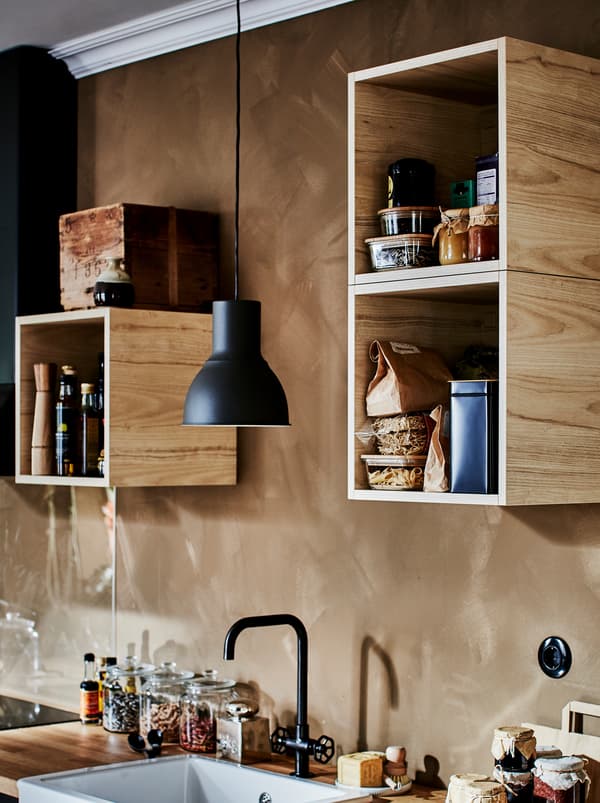 Armoires TUTEMO remplies d’accessoires de cuisine divers, réparties de façon irrégulière sur le mur au-dessus de la kitchenette.