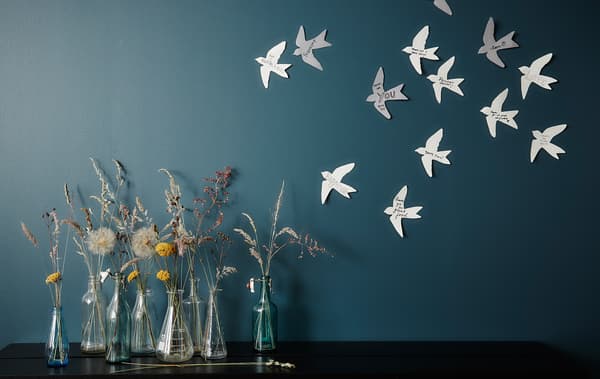 Arrangement de vases devant un mur décoré d'oiseaux en papier.