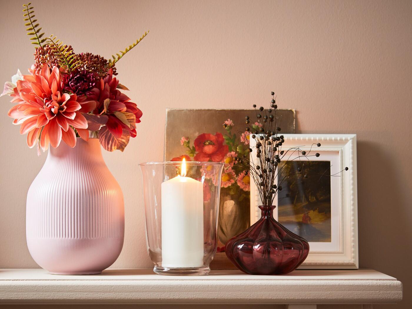 Artificial flowers in a vase, with a candle and photo frame.