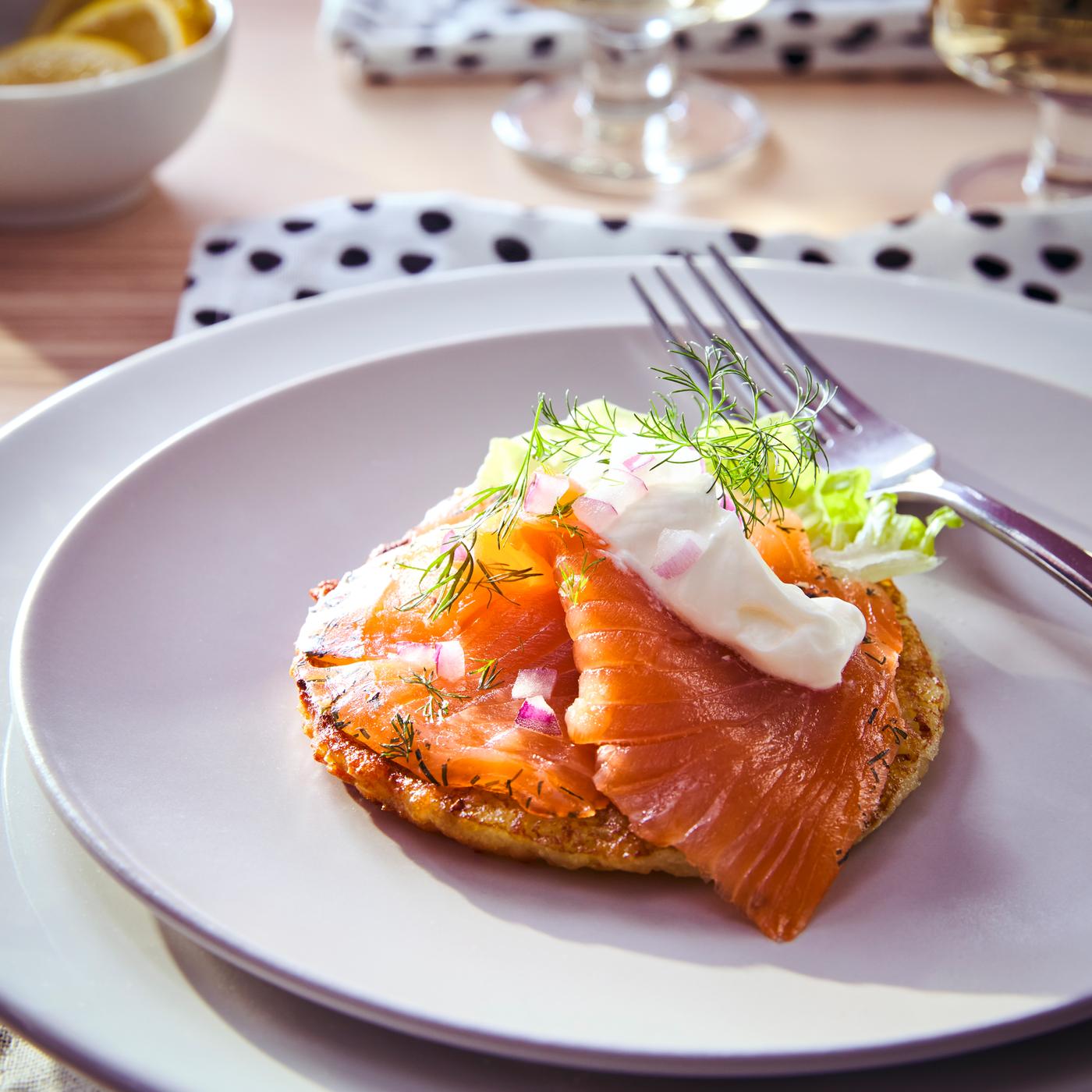ASC-certified SJÖRAPPORT cured cold smoked salmon dressed with dill, chopped onion and sauce on a white plate next to a fork.