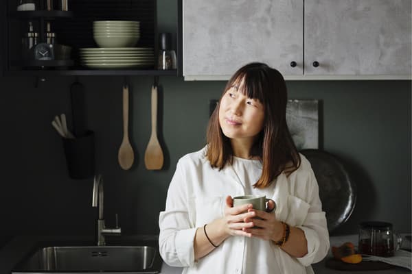 Asian woman holding a mug in her hand, in front of an IKEA kitchen. Customer is part of the IKEA Kitchen Referral Programme