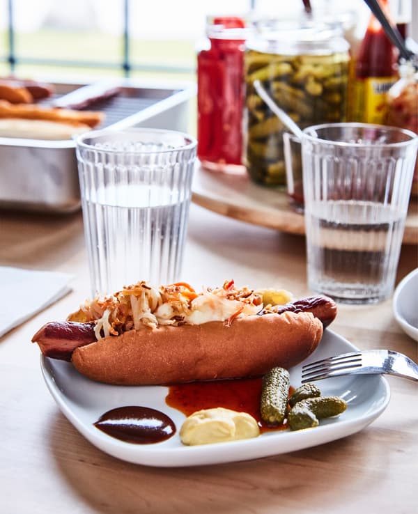 Assiette avec hot dog dans un petit pain et de nombreux accompagnements, le tout présenté sur une table.