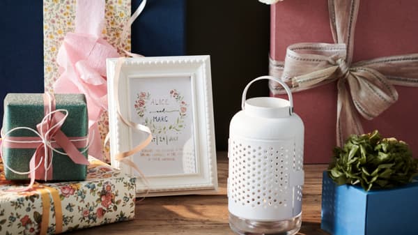 Assorted gift boxes wrapped in colorful paper and ribbons, a framed card with floral design, a white decorative lantern, and a small potted plant displayed on a wooden table.