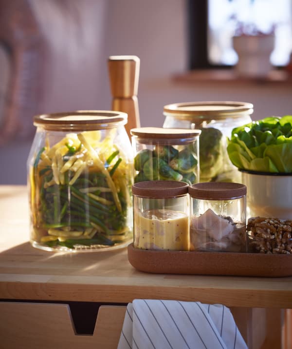 Assortment of small or side dishes – vegetables, herring and more – in different-size glass jars, placed on wooden surface.