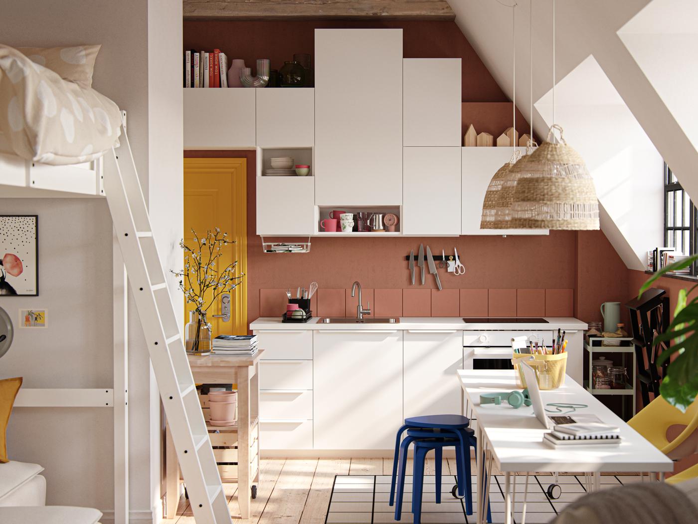 استوديو بسق مائل ونوافذ على الطراز الهندسي وجدران مطلية بلون الطين الغامق وواجهات مطبخ VALLSTENA باللون الأبيض.