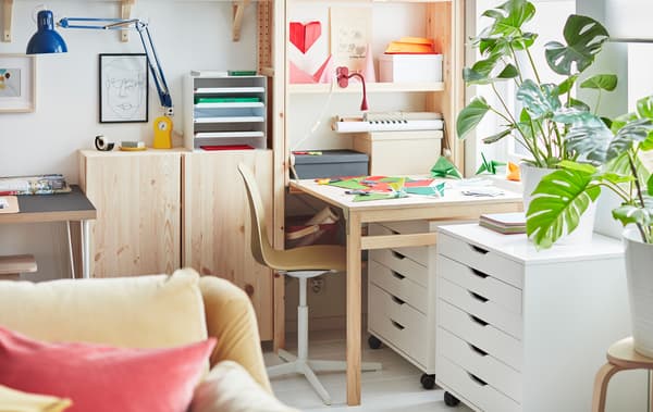 At one end of a wall-wide IVAR storage unit, a workspace created by a folded-out table, covered with coloured paper.