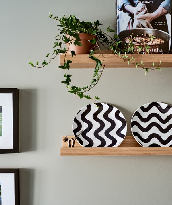 اثنان من رفوف الصور الخشبية، الرف السفلي عليه أطباق بيضاء بنقش أسود مُموّج، والعلوي عليه نبات لبلاب في إناء وكتاب طهي.