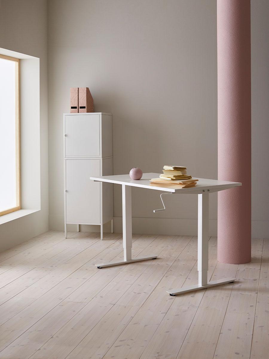 Au milieu d'une pièce nue, il y a un bureau blanc avec quelques livres et une armoire blanche avec deux magazines dessus.