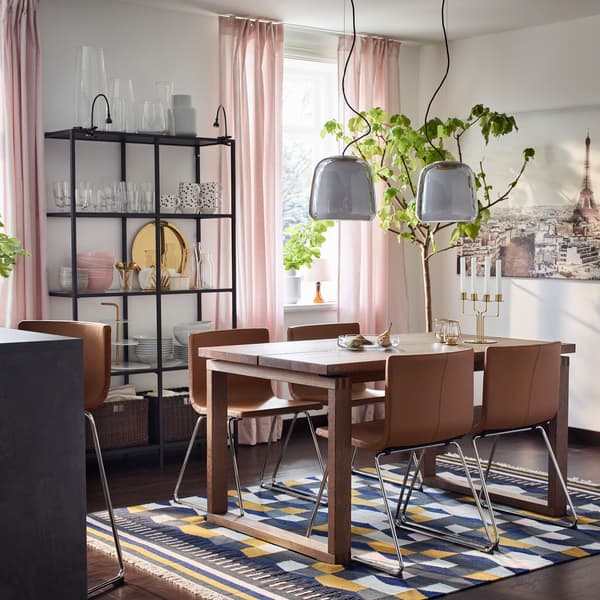 Avec leurs arêtes et leurs lignes droites, la table de salle à manger brune IKEA MÖRBYLÅNGA en placage de chêne et les chaises BERNHARD brun doré forment un duo moderne.