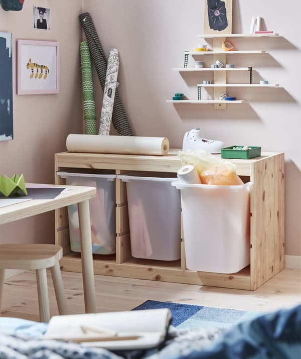 Bacs de rangement profonds dans un meuble en bois clair, avec des fournitures artistiques et des étagères au-dessus.