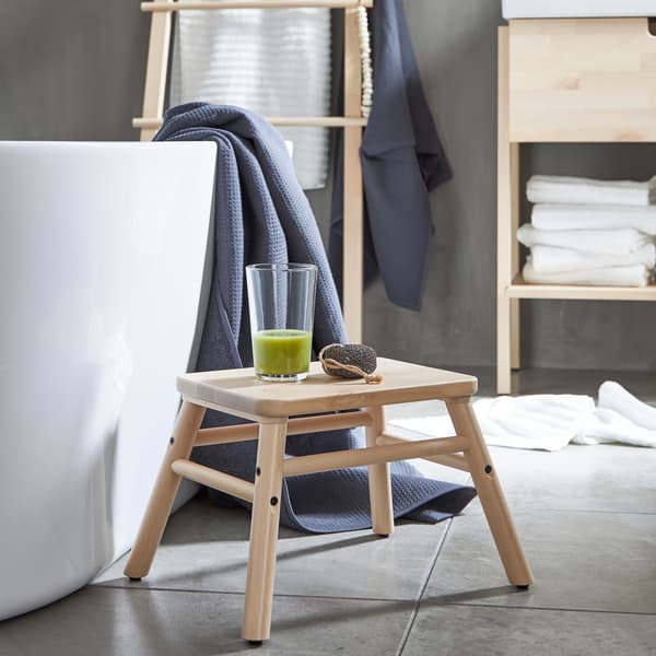 Bagno minimalista con scaletta/sgabello VILTO in betulla su cui è appoggiato un bicchiere di smoothie verde, accanto a una vasca da bagno.