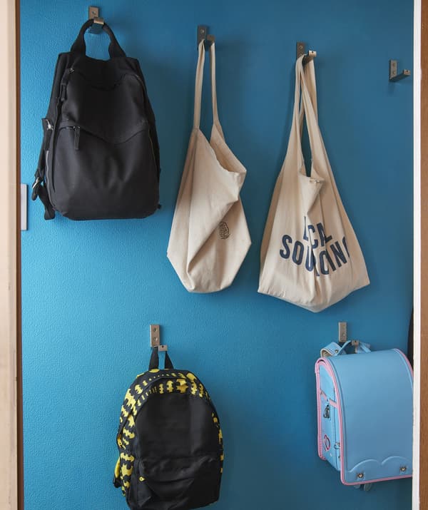 Bags and backpacks hang on hooks at different heights on a blue wall.