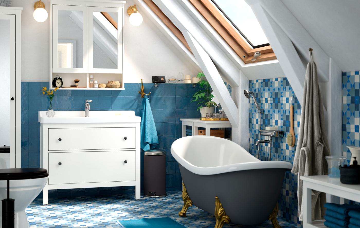 Baignoire sur pieds, meuble-lavabo blanc et armoire-pharmacie à portes miroirs dans une salle de bains à céramique bleue au mur et au plancher.