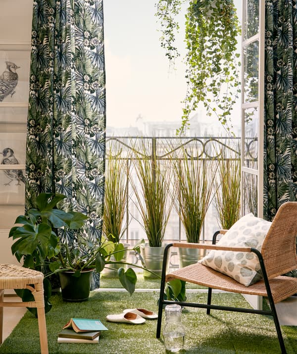 Balcon à la française et chaise au soleil, portes ouvertes encadrées par des plantes suspendues et en pot, textiles verts et gazon artificiel.
