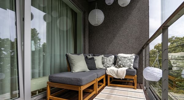 Balcony corner with wooden lounge furniture and decorative pillows.