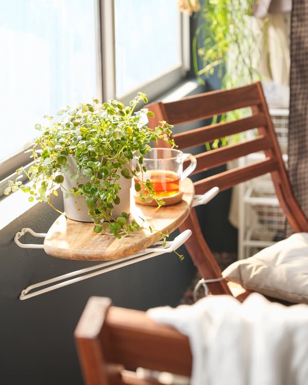 Balcony with a minute sideboard created by a chopping board placed on SKRÄLL hooks; tea and a plant pot on it, chairs beside.