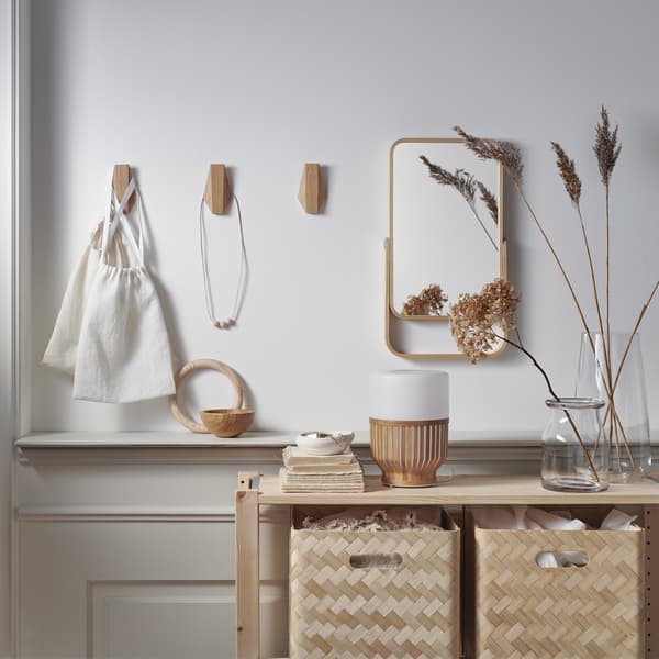 Bamboo storage boxes in a wooden unit, a mirror and wooden hooks on a white wall.