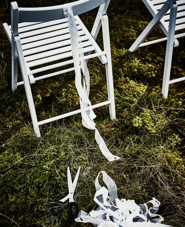 Bandelette découpée dans un filet SOLIG et nouée au dos d’une chaise pliante blanche 