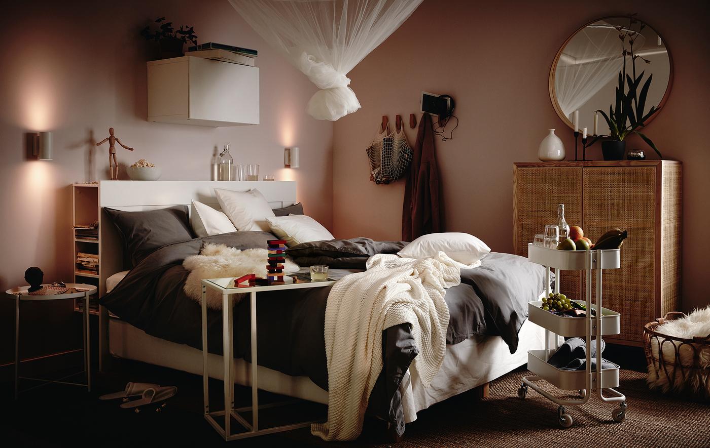 Bed laden with fluffy bedding, cushions and throws, trolley with snacks and drinks beside it, and a net in a knot hanging above.
