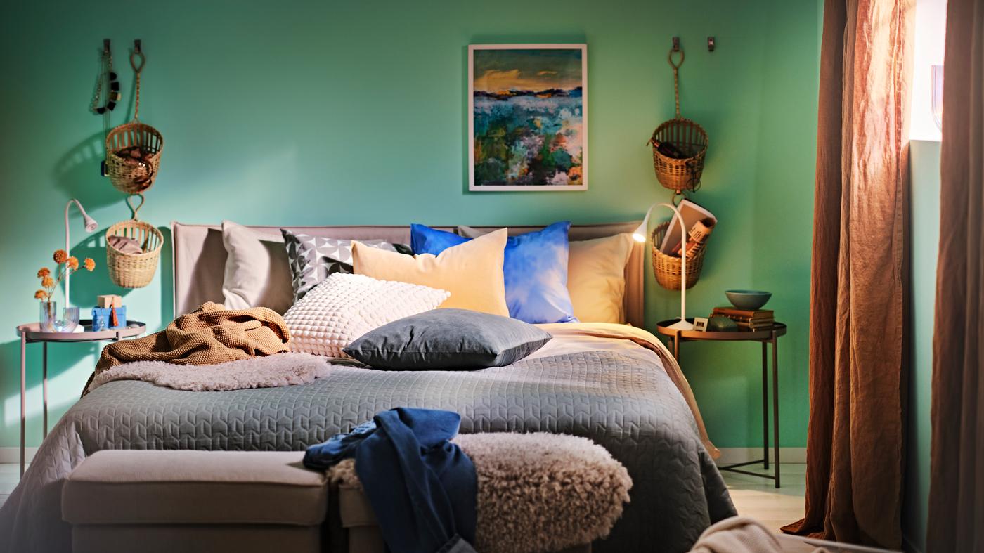 Bed met KLEPPSTAD bedframe in wit/beige opgemaakt met een grijsgroene sprei en verschillende kussens, plus twee tafeltjes met dienblad.