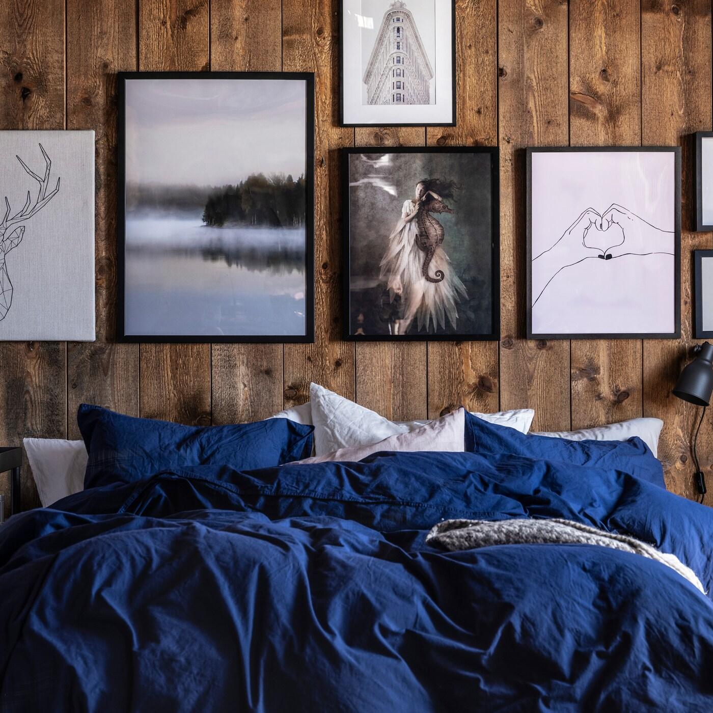 Bed with blue and white bedding and rustic wooden wall decorated with artworks in black, white and grey tints.