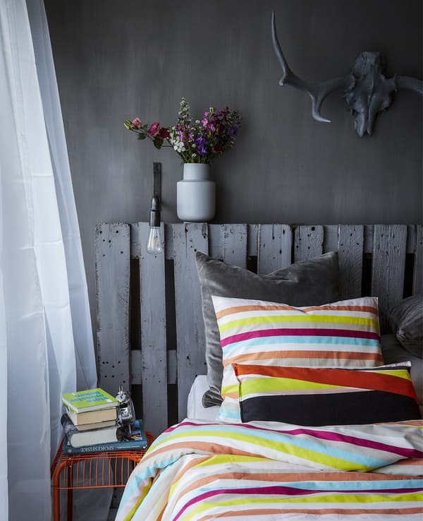 Bed with multi-coloured bedding against grey background decor.