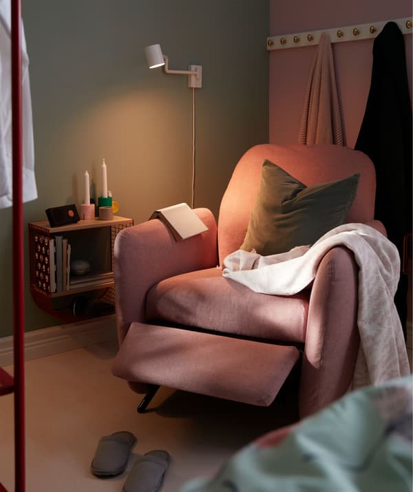 Bedroom corner between bed and a room divider with a recliner, wall-mounted reading light and a small wall shelf.