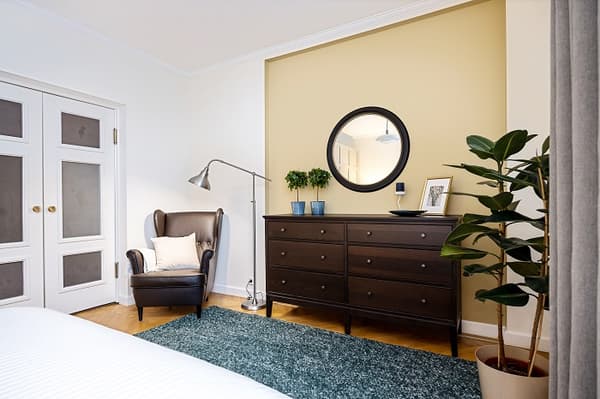 Bedroom dresser with round mirror, indoor plants, and leather armchair