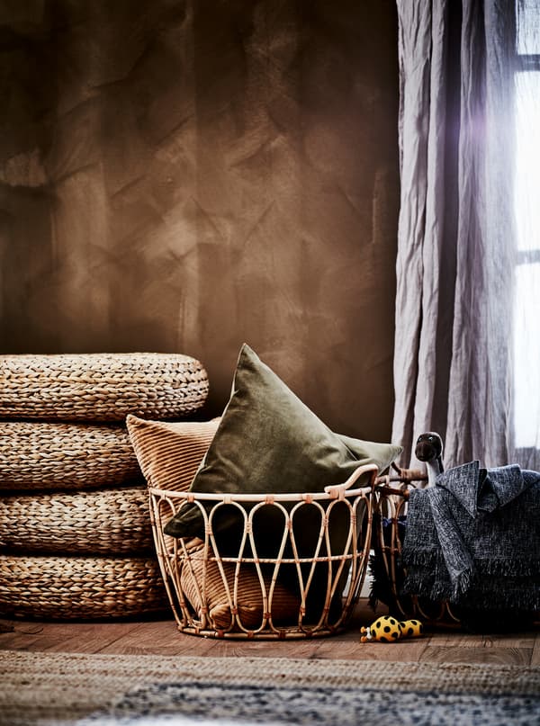 Bedroom section in earthy colours, featuring SNIDAD rattan basket with textiles, stacked ALSEDA stools and rugs in natural materials.