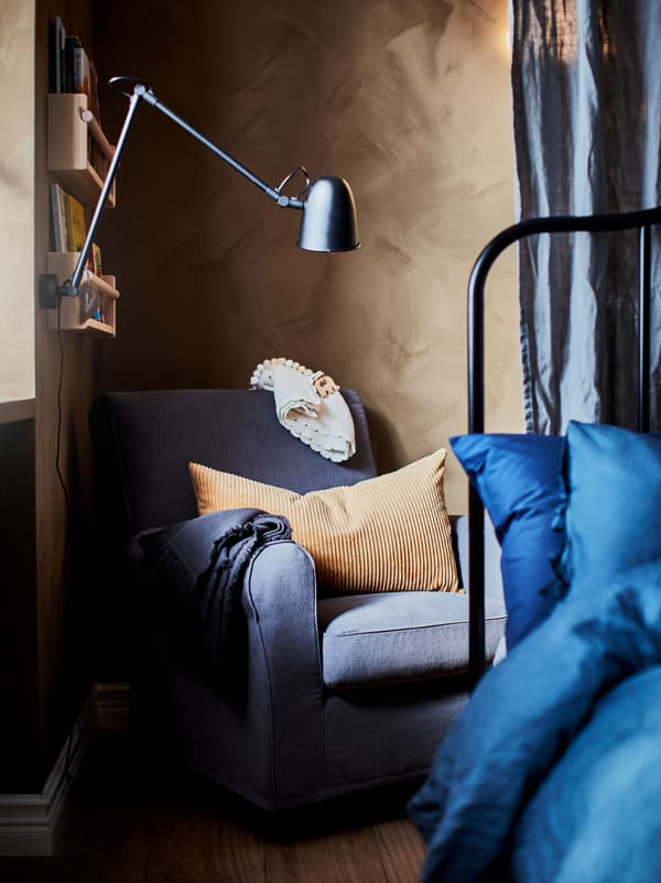 Bedroom with a GRÖNLID armchair standing in a corner behind the main bed. Above hangs a shelf-mounted work lamp.