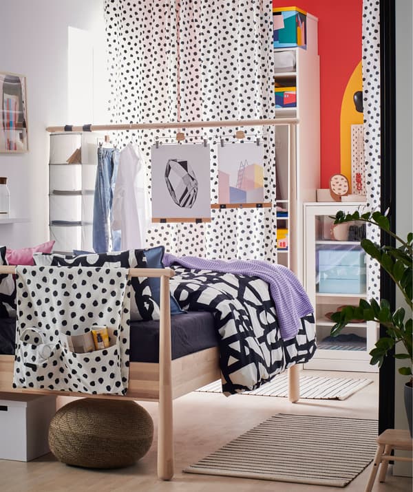 Bedroom with the far wall, behind curtains, covered with open and closed storage. The high headboard of a bed acts as room divider.