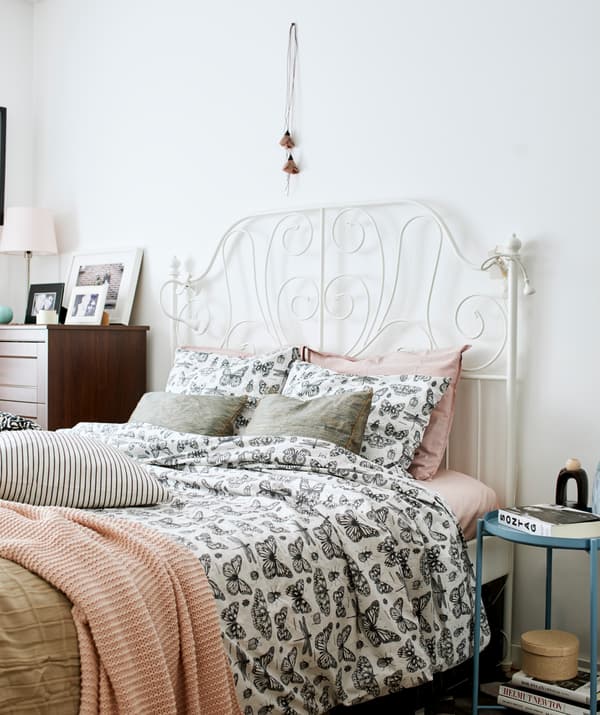 Bedroom with white, wrought-iron bed made up with butterfly-patterned bedding and pink covers, and dark wood drawers.