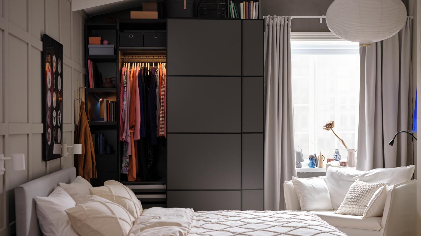 Behind a bed is a dark grey PAX/MEHAMN wardrobe with the left sliding door slightly open, showing clothes hanging on a rail.