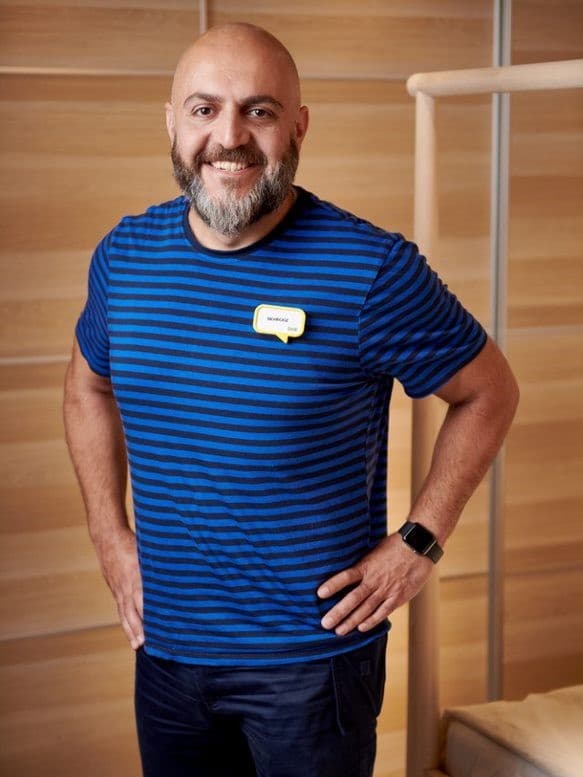 Behrooz i en blå IKEA t-shirt foran et skab med skydelåger i træ.