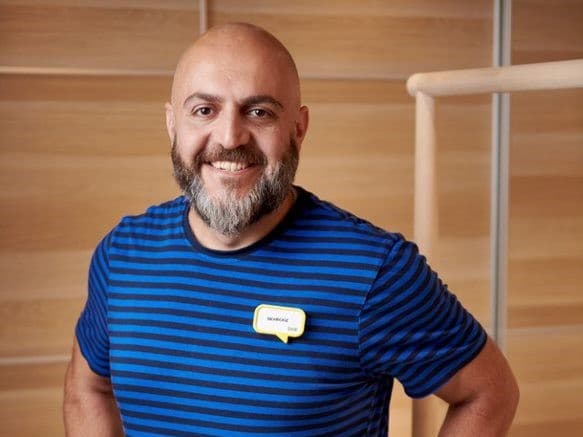 Behrooz i en blå IKEA t-shirt foran et skab med skydelåger i træ.