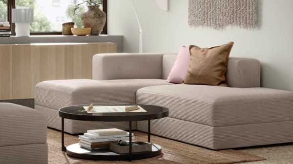 Beige JÄTTEBO modular sofa with chaise lounge in a modern living room, styled with pink and tan cushions and a round black coffee table.
