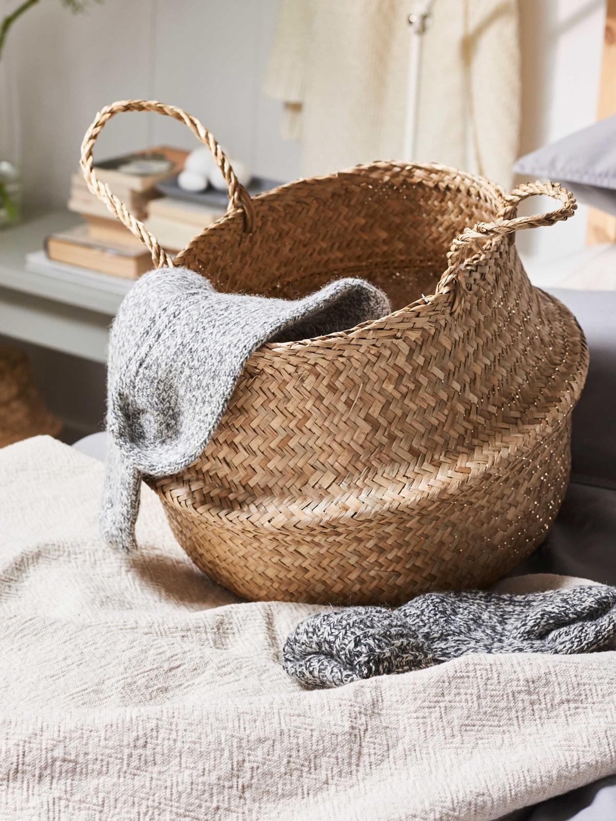 Beige seagrass basket on a bed with a pair of grey socks inside.