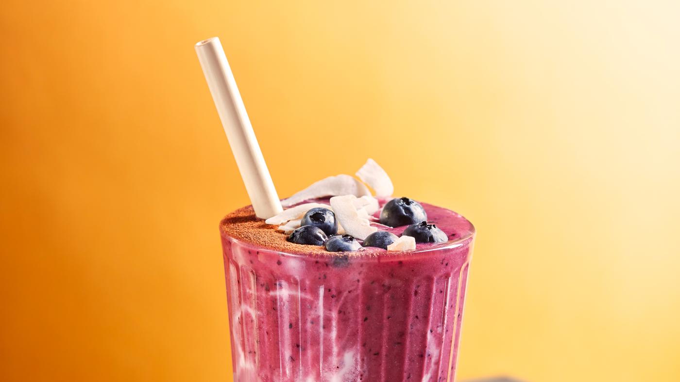 Bicchiere rosa e bianco con cannuccia bianca contenente smoothie alla barbabietola e latte d’avena, decorato con mirtilli e scaglie di cocco - IKEA