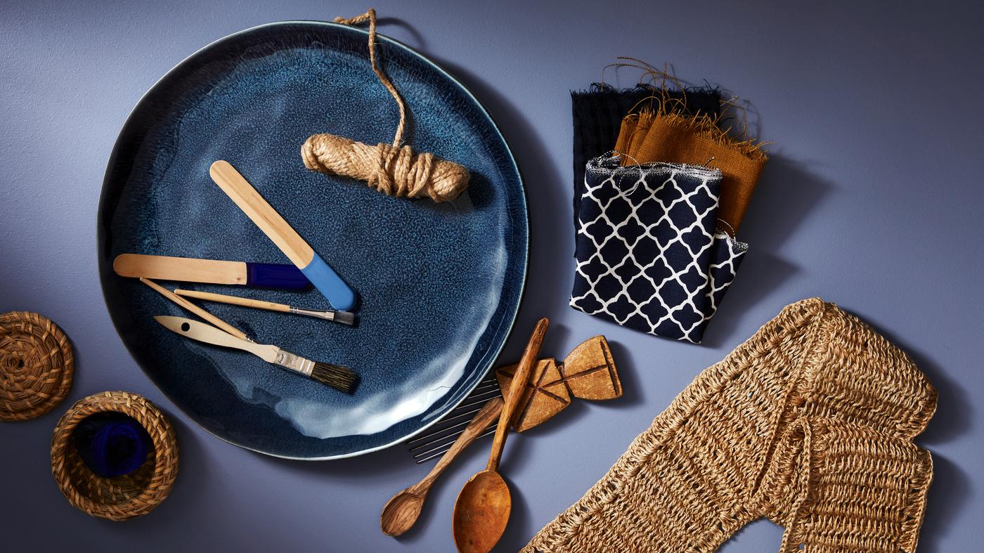 Big blue plate holding paint samples and paint brushes, beside fabric samples and wooden spoons.