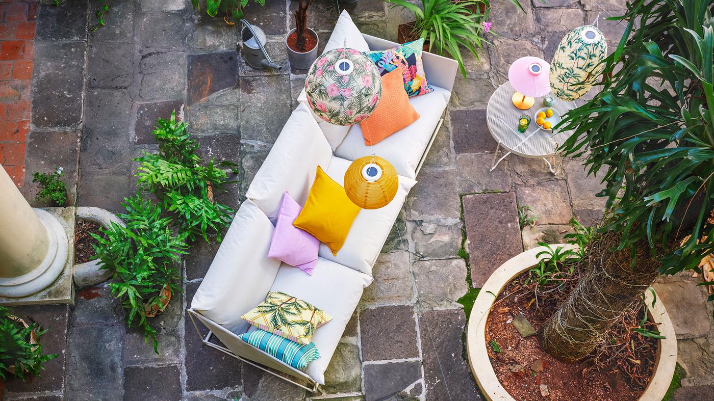 Bird's eye view of an outdoor space with a comfortable sofa, colourful cushions and lanterns, and several flourishing plants.
