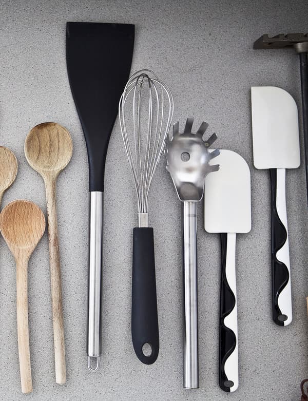 Bird's-eye view of kitchen utensils on a grey surface. Includes wooden spoons, and black and white spatulas.